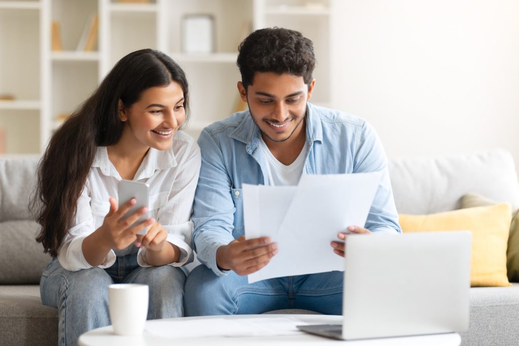 Young Indian couple reviewing document, with laptop and coffee